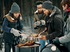 Four people stood around a BBQ in winter weather cooking fish and poultry